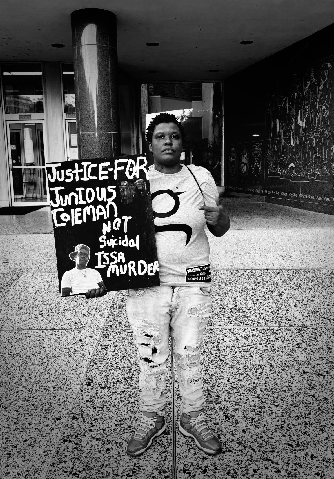 A protester stands with a sign demanding justice for Junious Coleman. Coleman's death was wrongfully ruled a suicide after he was shot outside New Orleans East Public Library in November 2022.