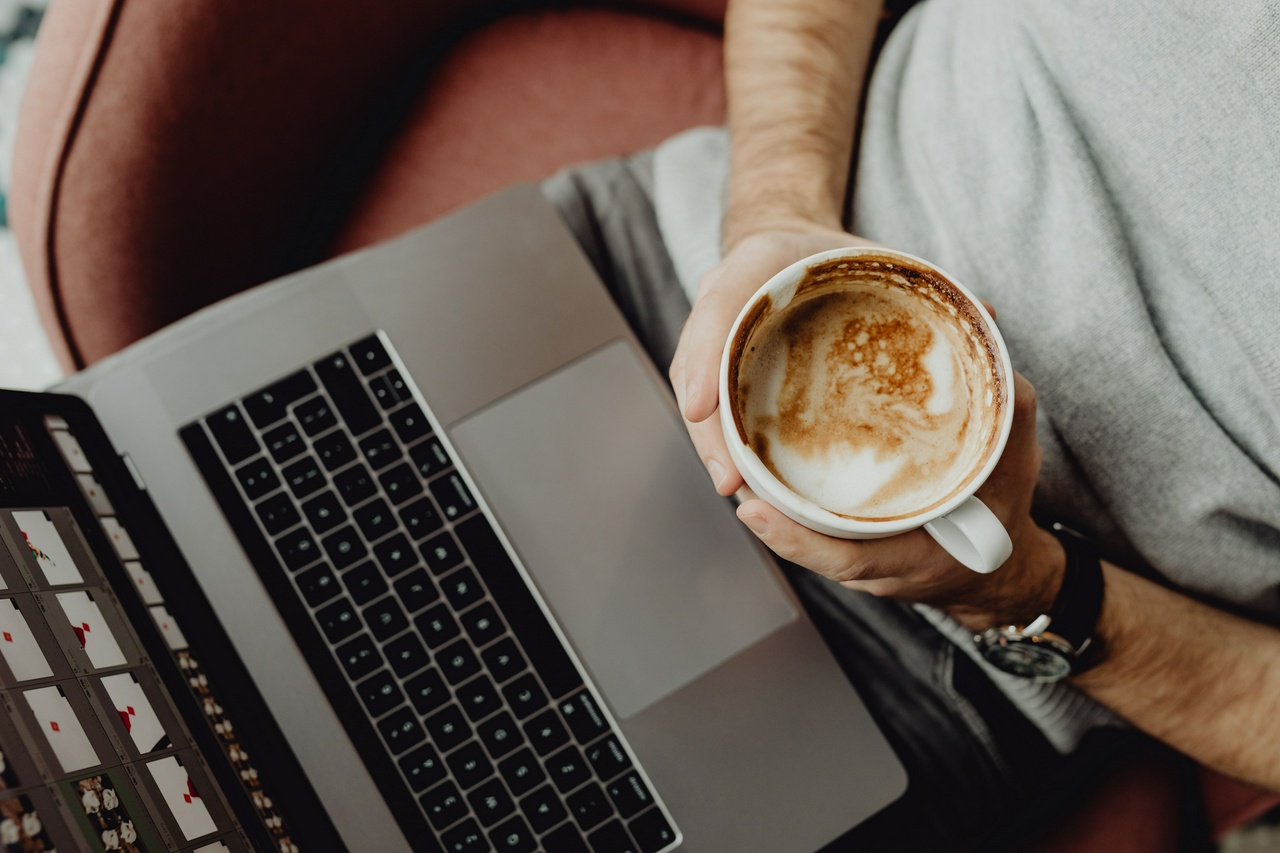 A man's hand is shown holding a coffee cup near a computer