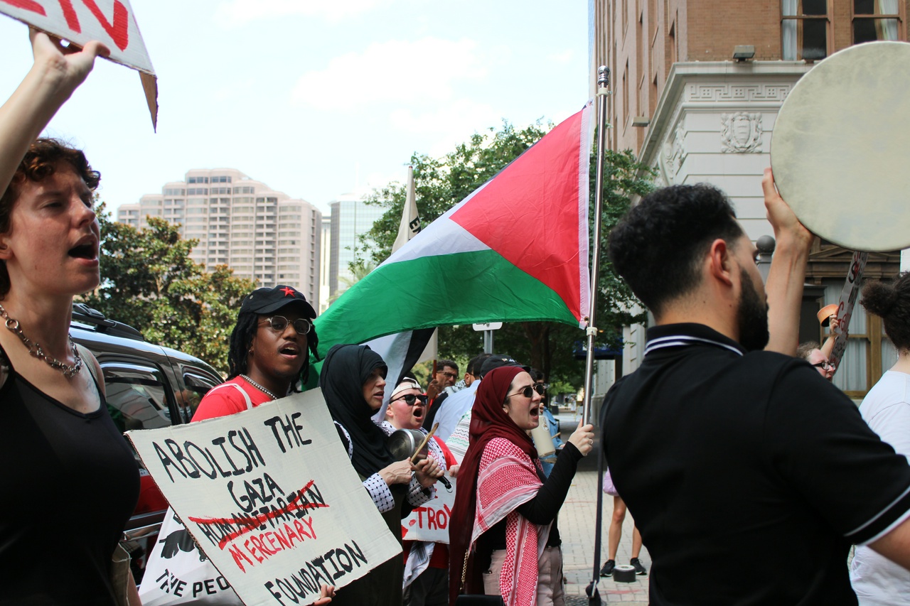 A group of protesters chanting and signs, flags, and drums.